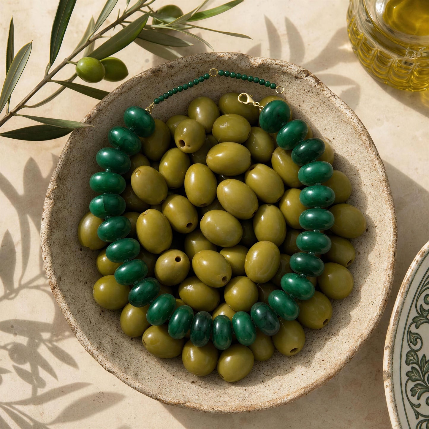 The Capri Verde Statement Choker in a bowl with olive branches and oil in the background
