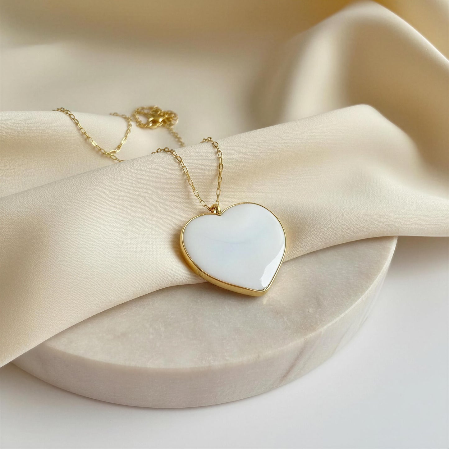 Heart-shaped pendant necklace with gold chain on beige fabric