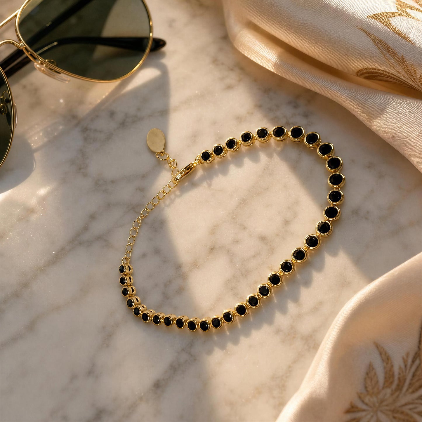 The Siena Black Tennis bracelet next to sunglasses and cream satin fabric in the background.