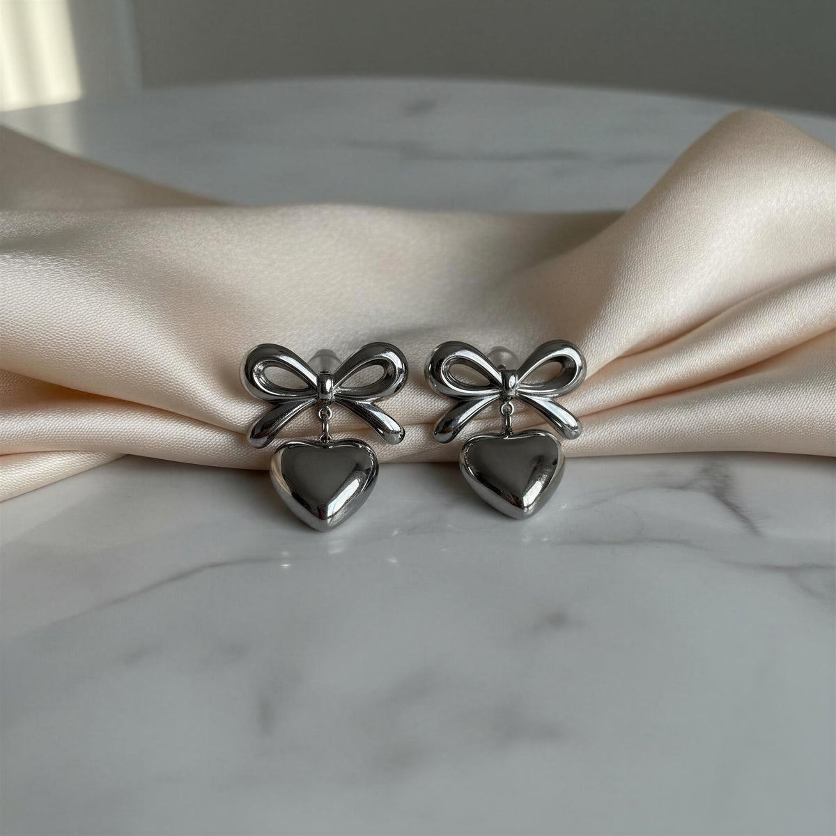The Cupid's Knot Earrings - Silver against marble table with vanilla color scarf
