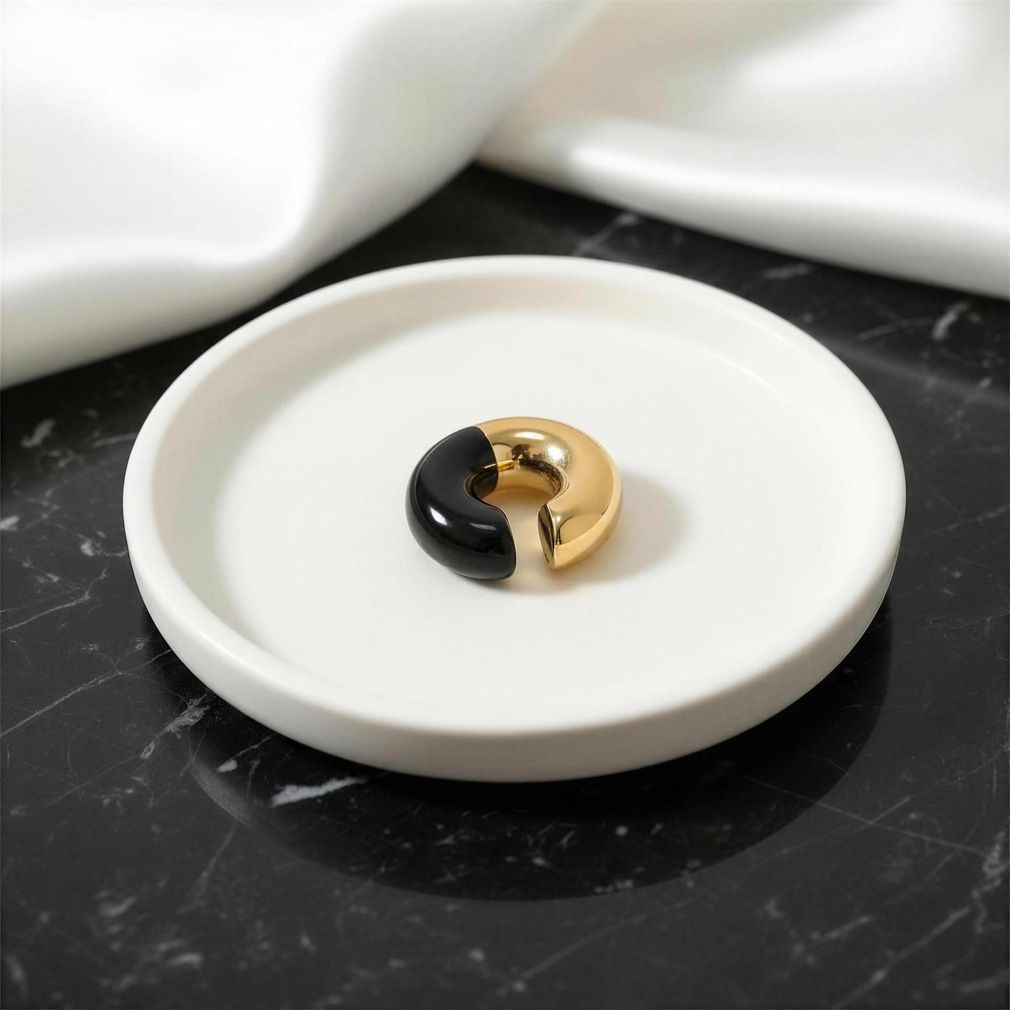 Gold and black ear cuff on a white marble coaster with a black marble surface.