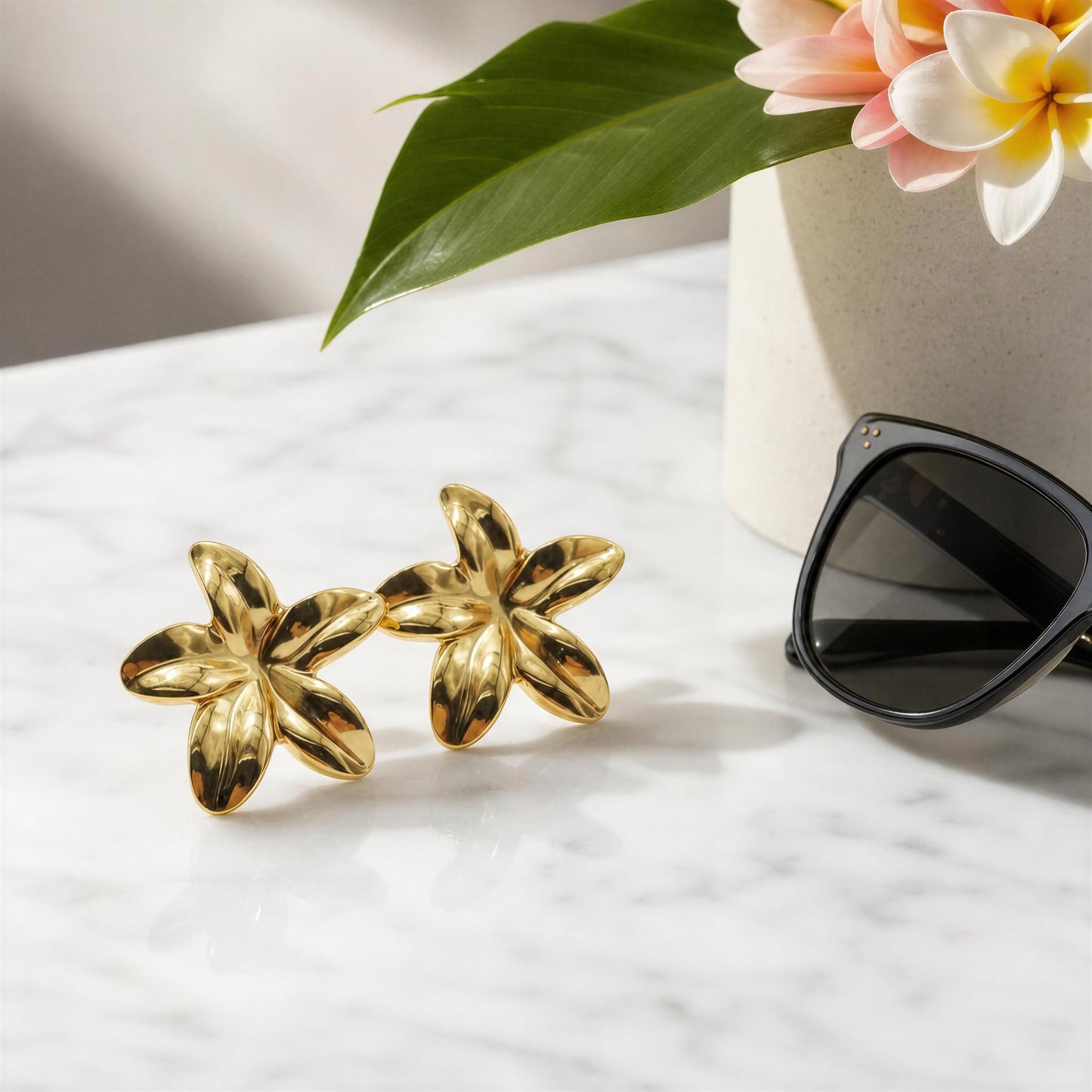 The Luna Bloom Earrings - Gold on a marble surface with sunglasses and flowers in the background