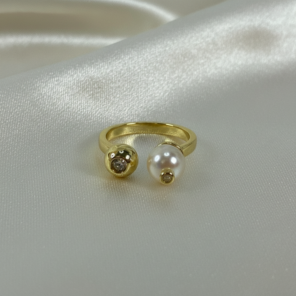 Gold ring with a pearl and small gemstone on a white satin background