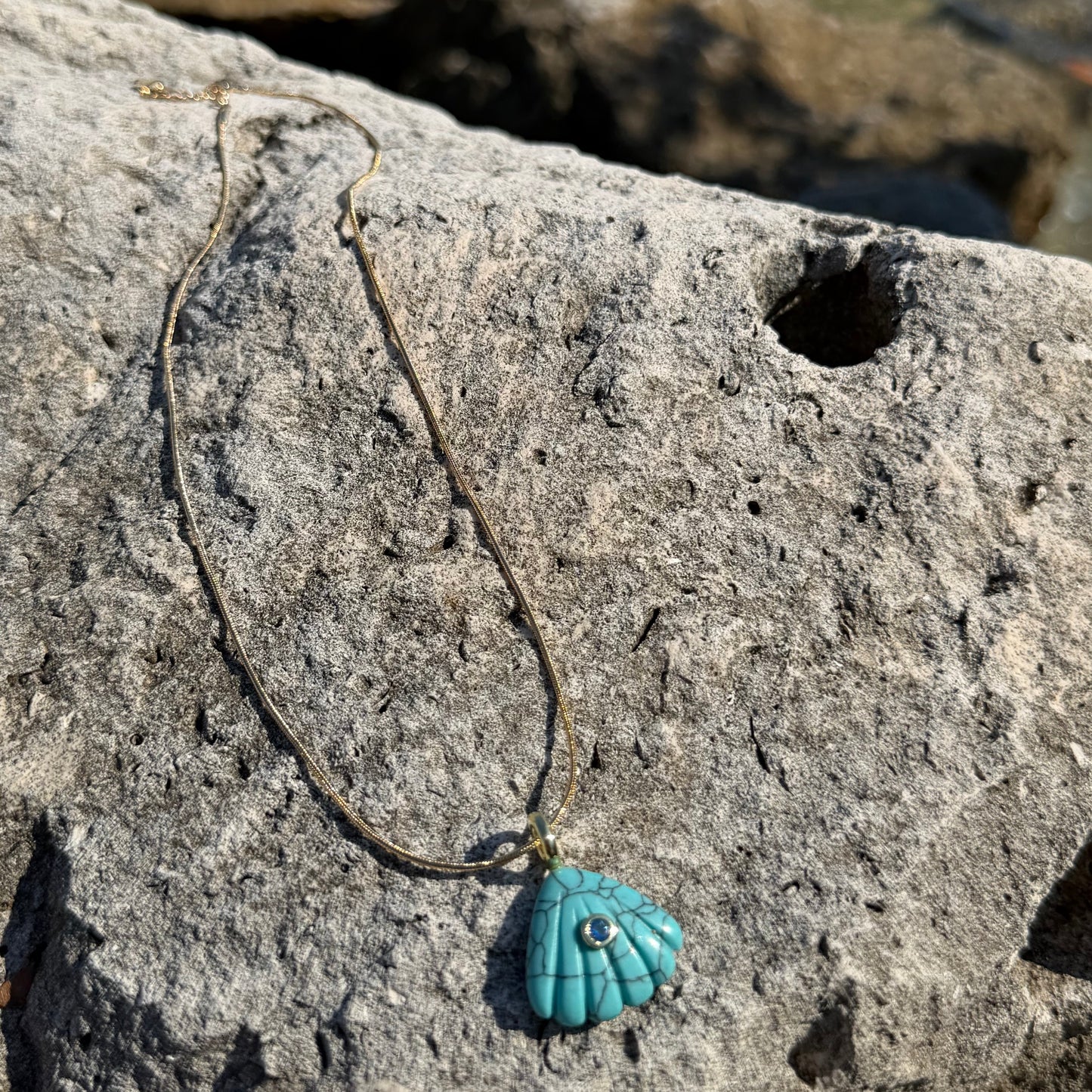 Beach styled turquoise shell necklace on rock near water