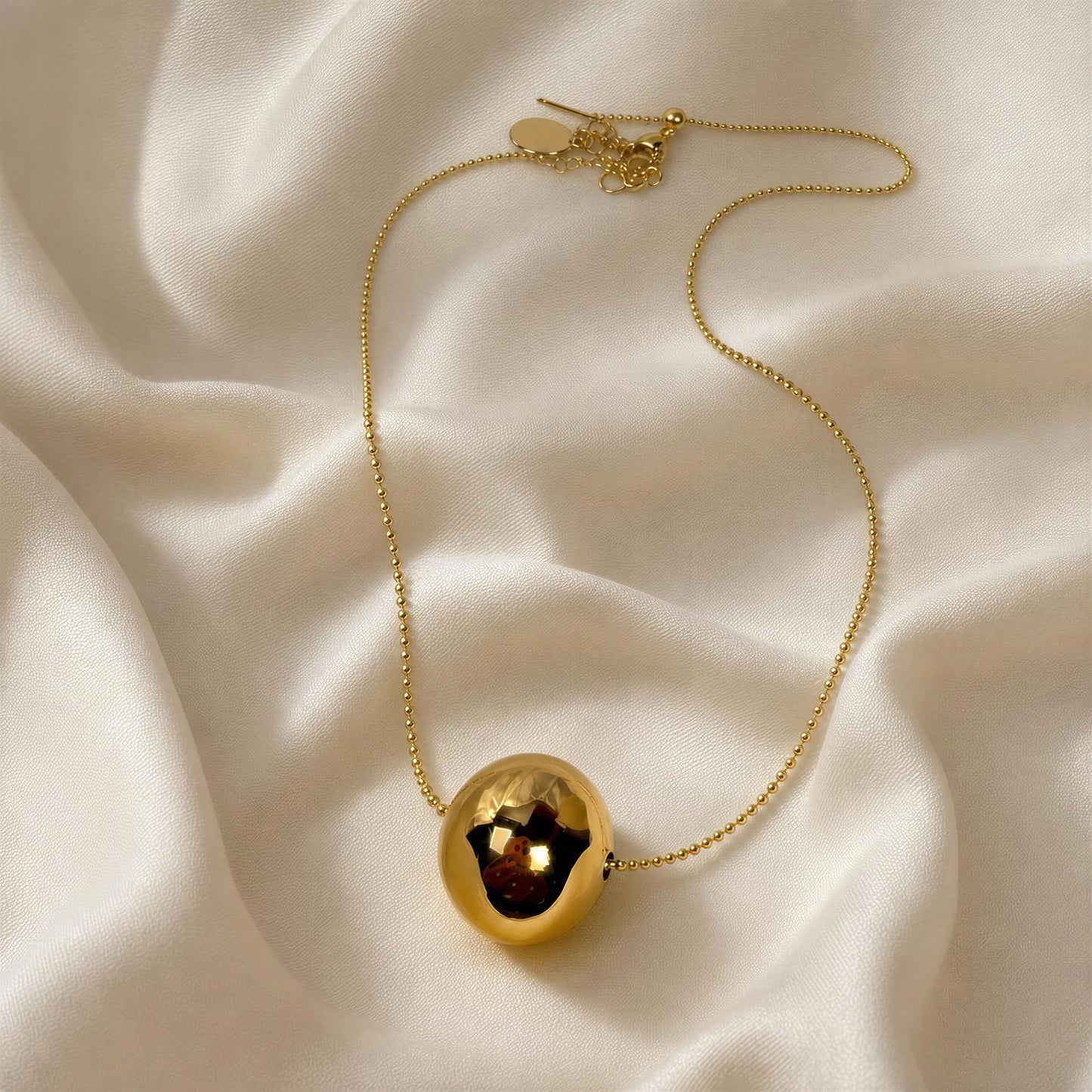 Gold necklace with a spherical pendant on a beige fabric background