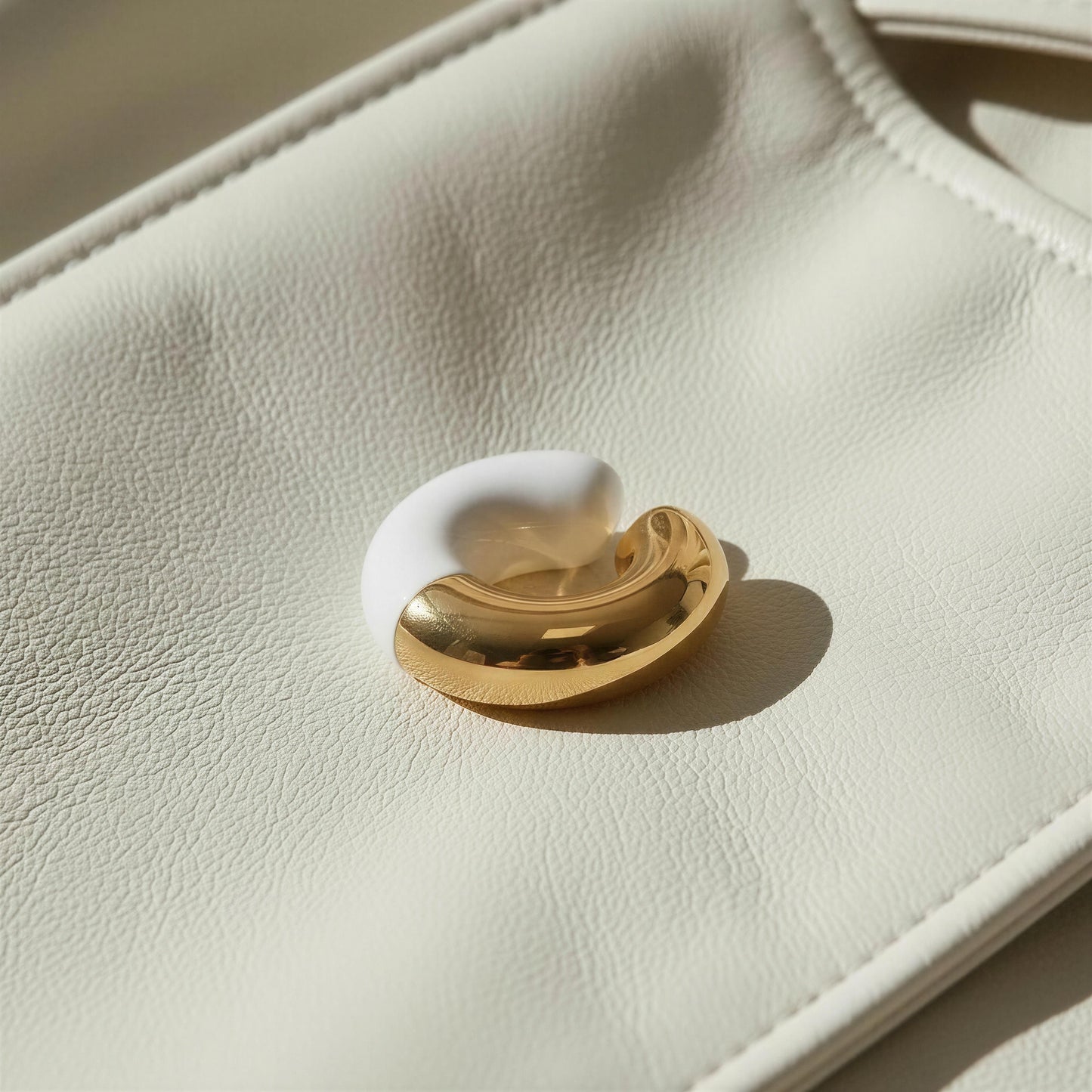 Close-up of a white and gold ear cuff on a beige leather surface