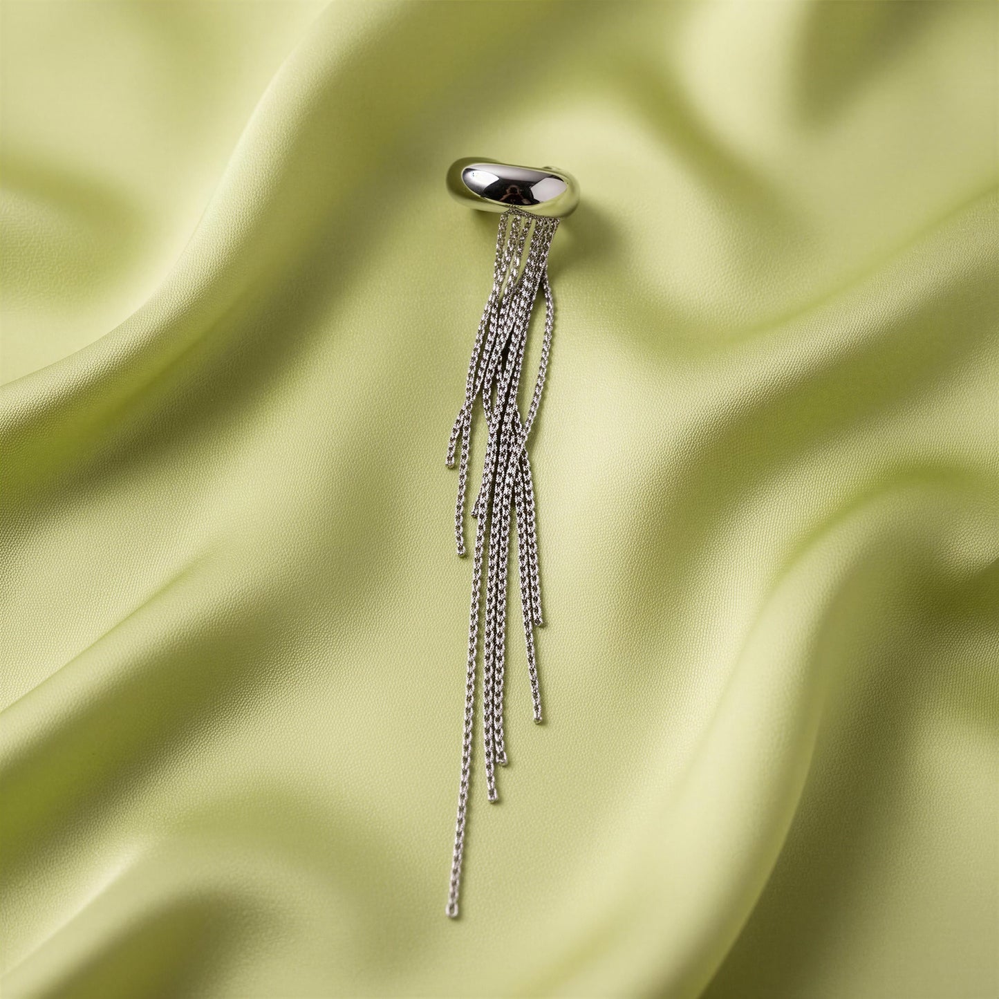 The Vela Silver Ear Cuff on a light green satin background
