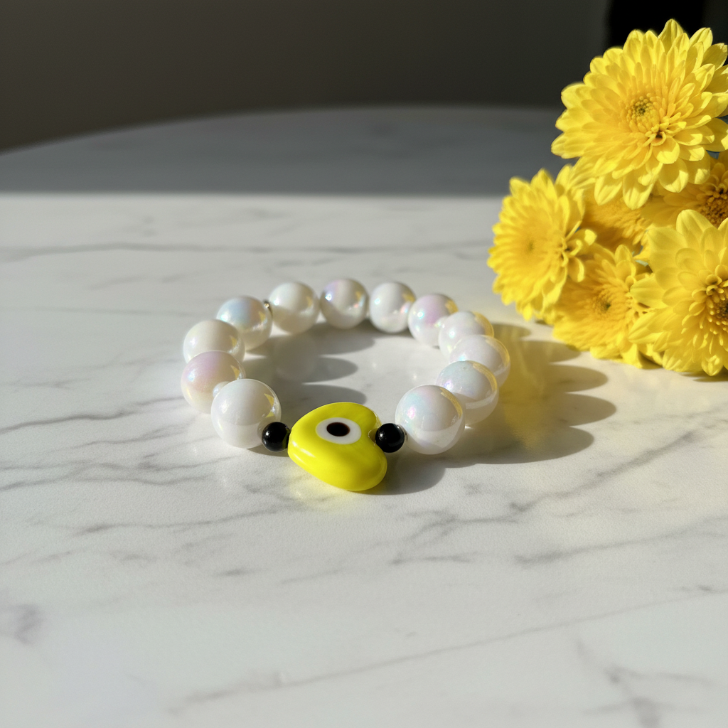 Aegis Sol Heart Bracelet with yellow guardian eye charm next to yellow flowers on a marble surface