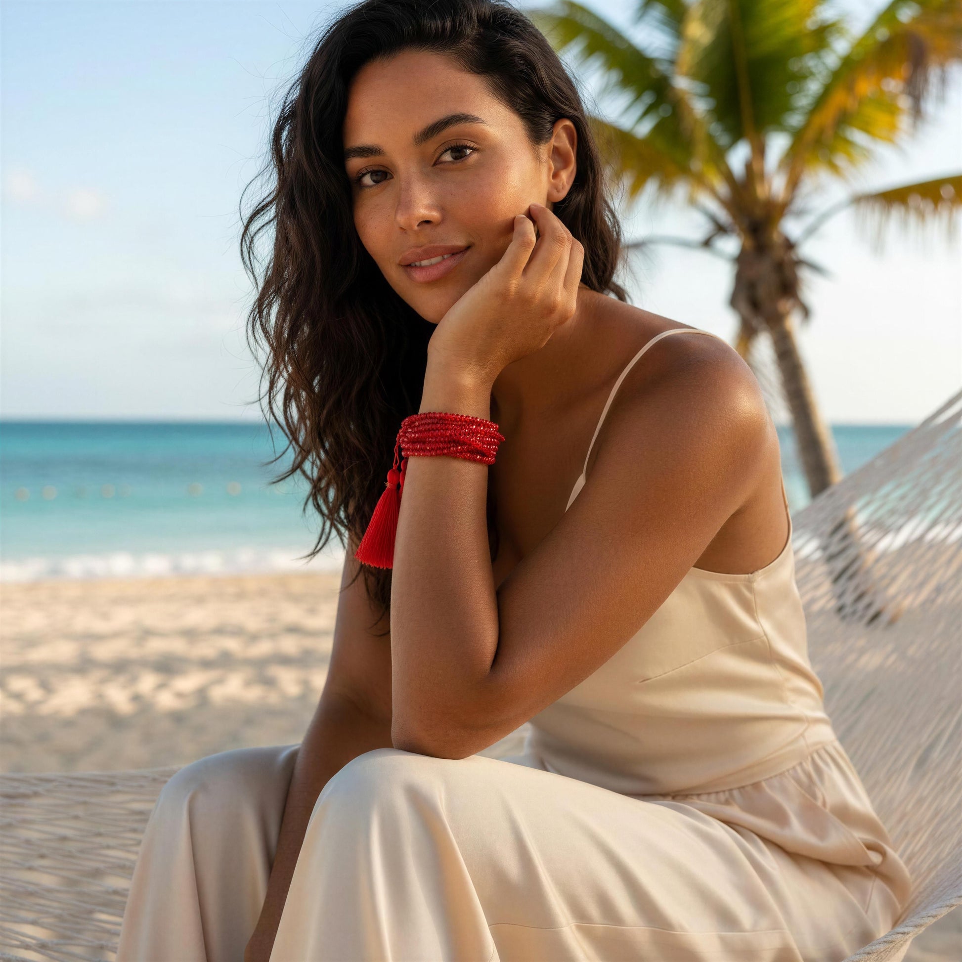 Woman sitting in a hammock on a beach with palm trees and ocean in the background wearing the Amarra Bracelet