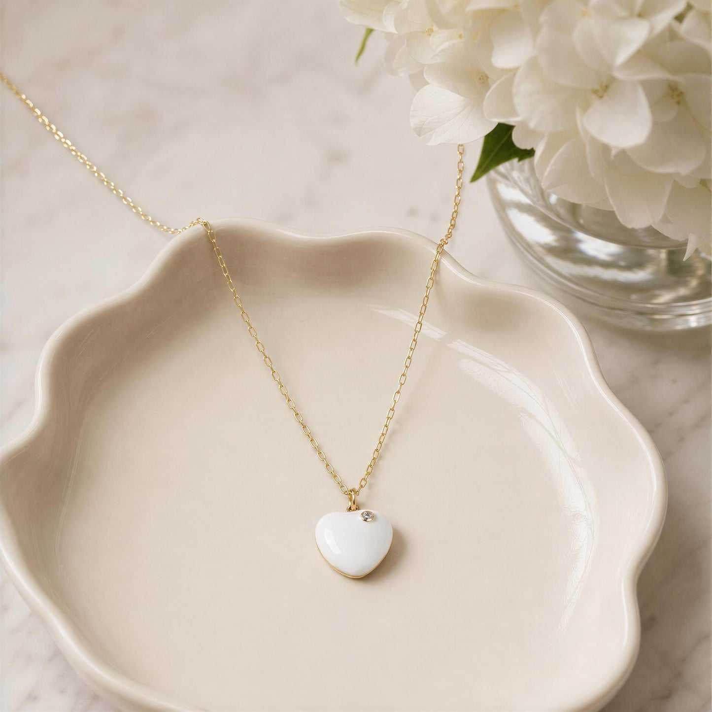 Gold necklace with a heart-shaped pendant on a white dish with flowers in the background