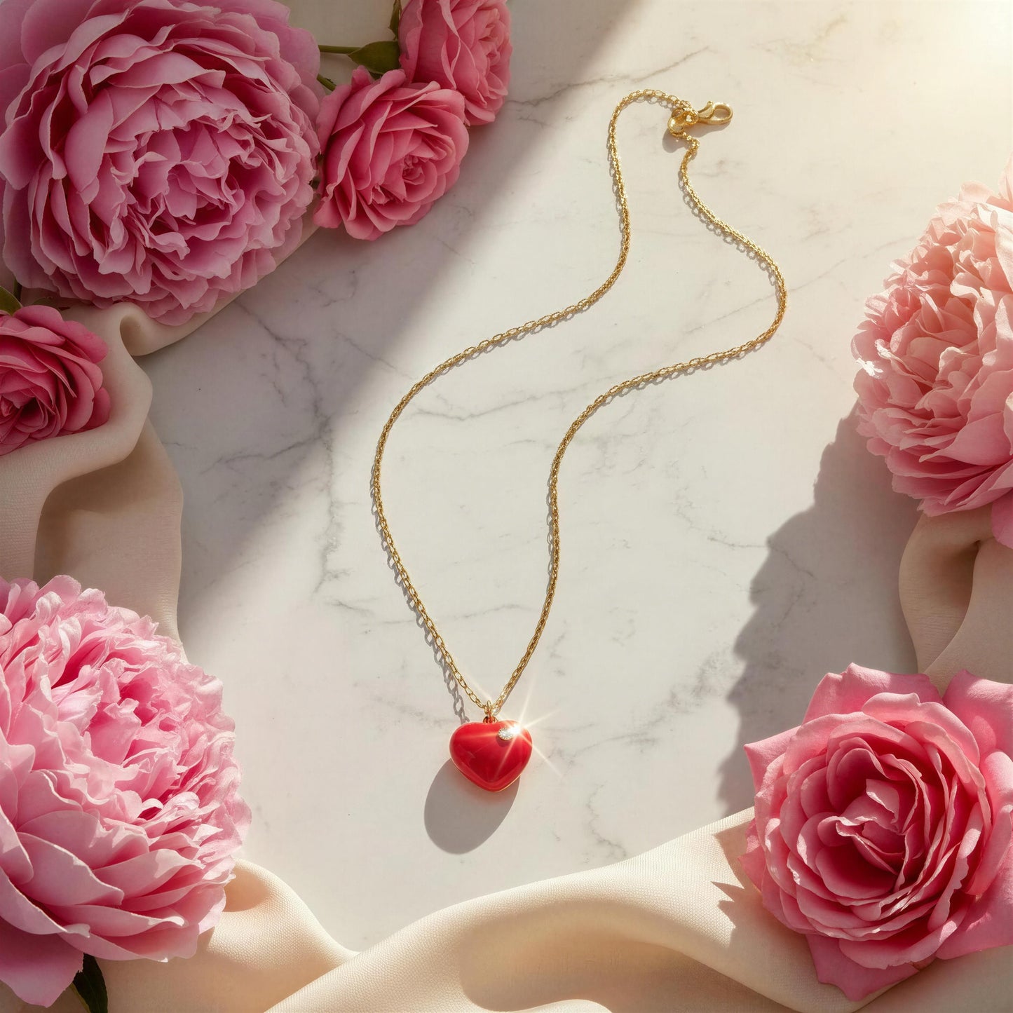 Gold necklace with a fuchsia heart pendant surrounded by pink roses on a marble surface