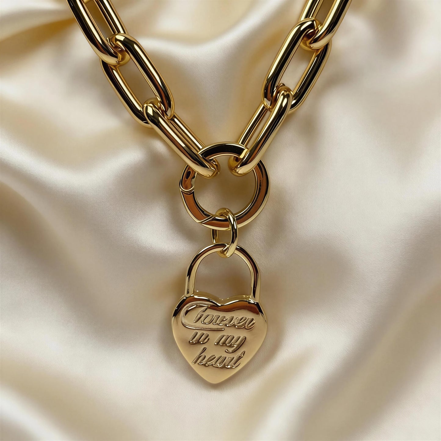 Gold chain necklace with a heart-shaped padlock charm on a beige fabric background