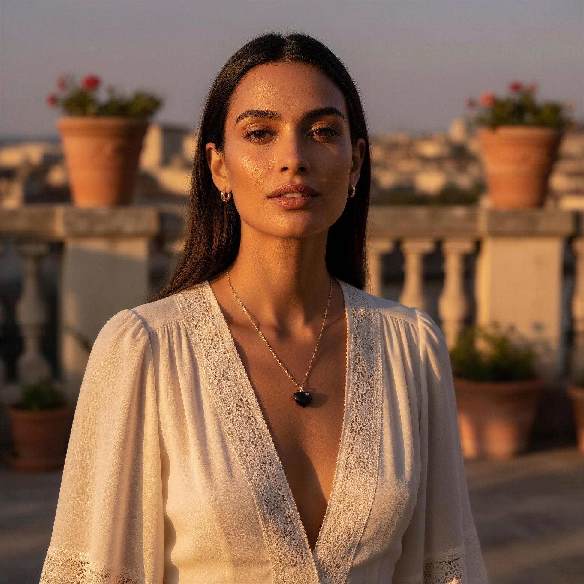 Woman in a white lace top on a rooftop with sunset lighting wearing the Amore Noir Heart Necklace.