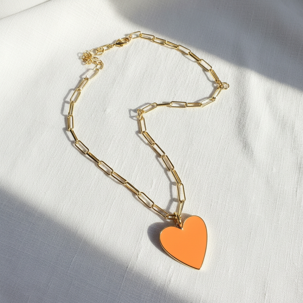 Gold chain necklace with an orange heart pendant on a white fabric background