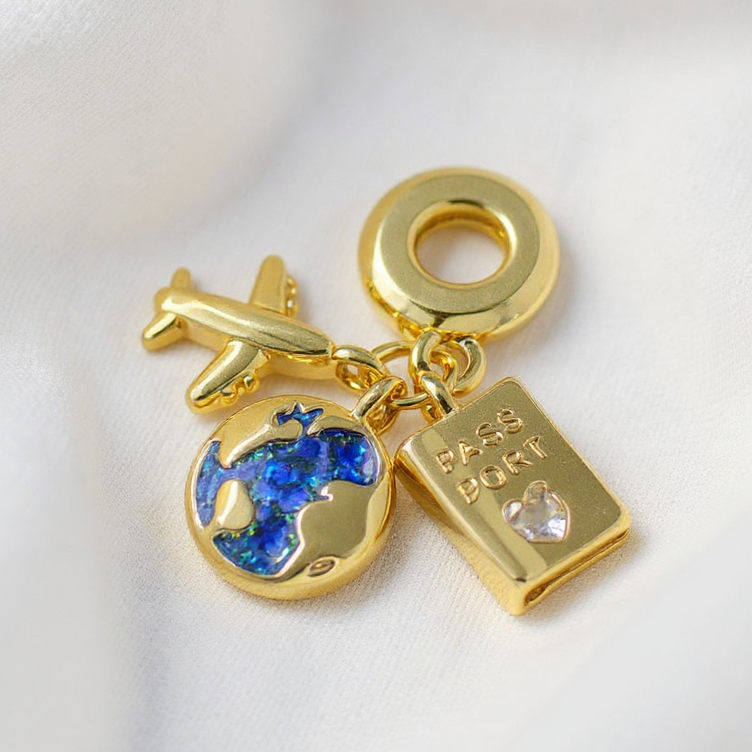 Gold charm with airplane, globe, and book on a white background