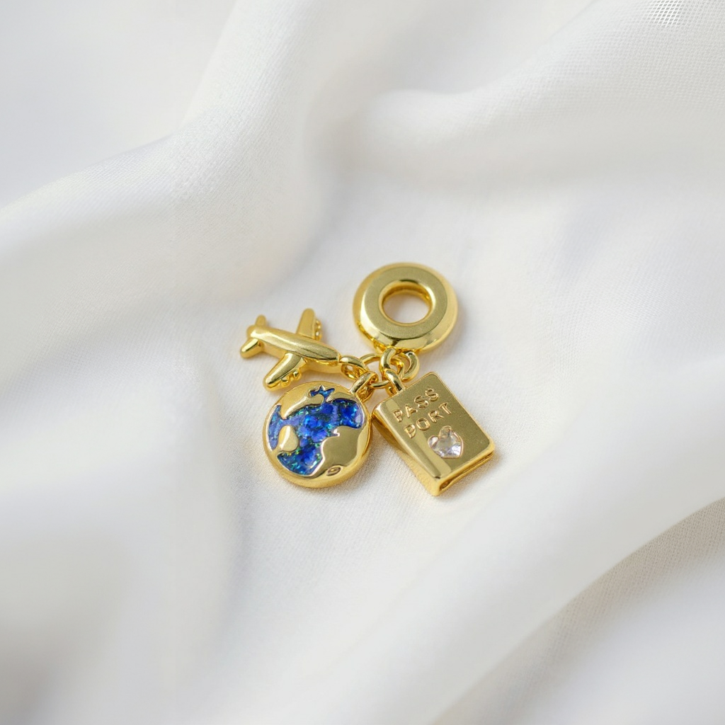 Gold charm with airplane, globe, and book on a white fabric background