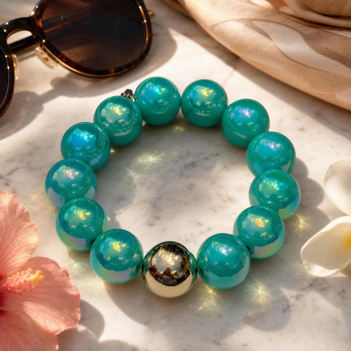 The Aquamarine Glow Bracelet on a marble surface with sunglasses and flowers.