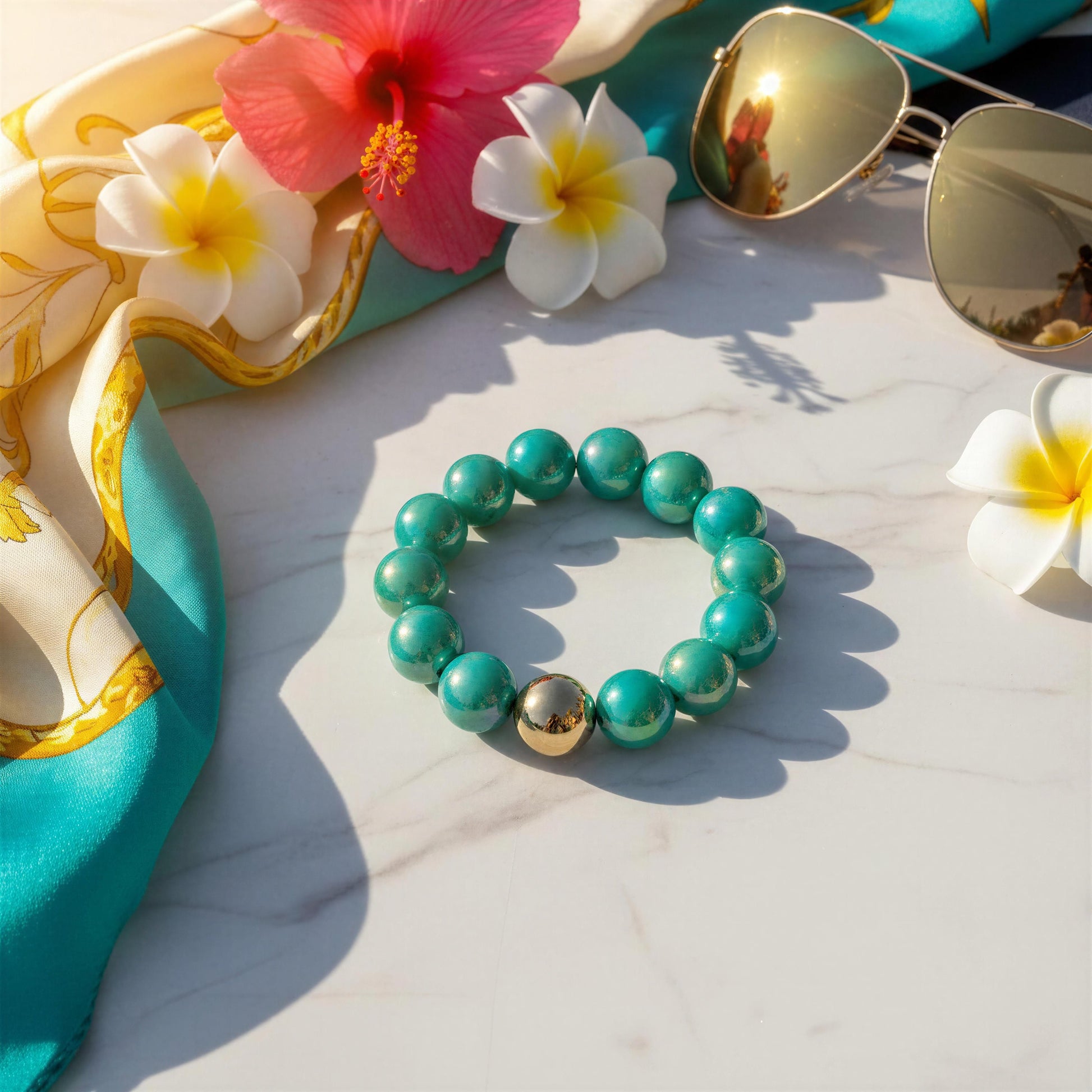 Turquoise beaded bracelet with gold accents on a white surface with flowers and sunglasses.