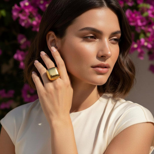 A woman wearing the Aurelia Ring from Chica Chica Jewelry, posing outdoors with blurred pink flowers in the background.