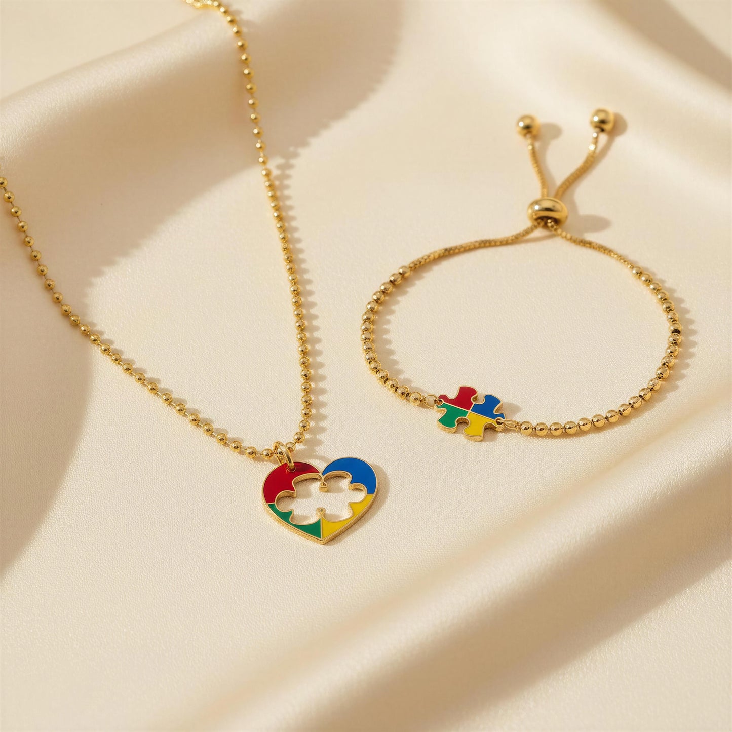 Gold necklace and bracelet with colorful heart and puzzle piece charms on a beige fabric background