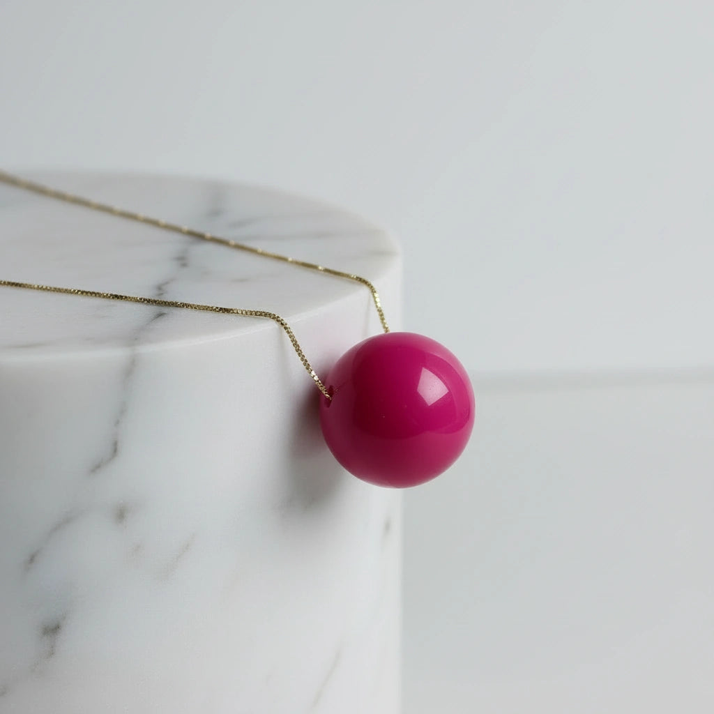 Azalea Sphere Statement Necklace with a pink bead on a marble surface