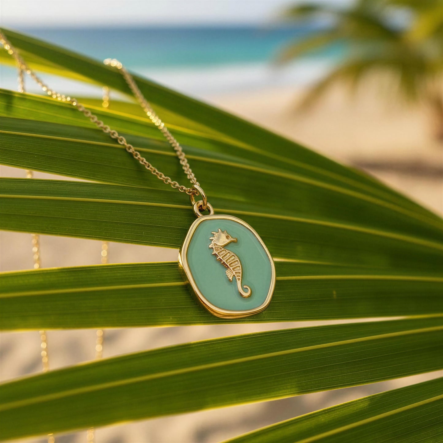 The Azure Seahorse Necklace on a palm leaf with a beach in the background