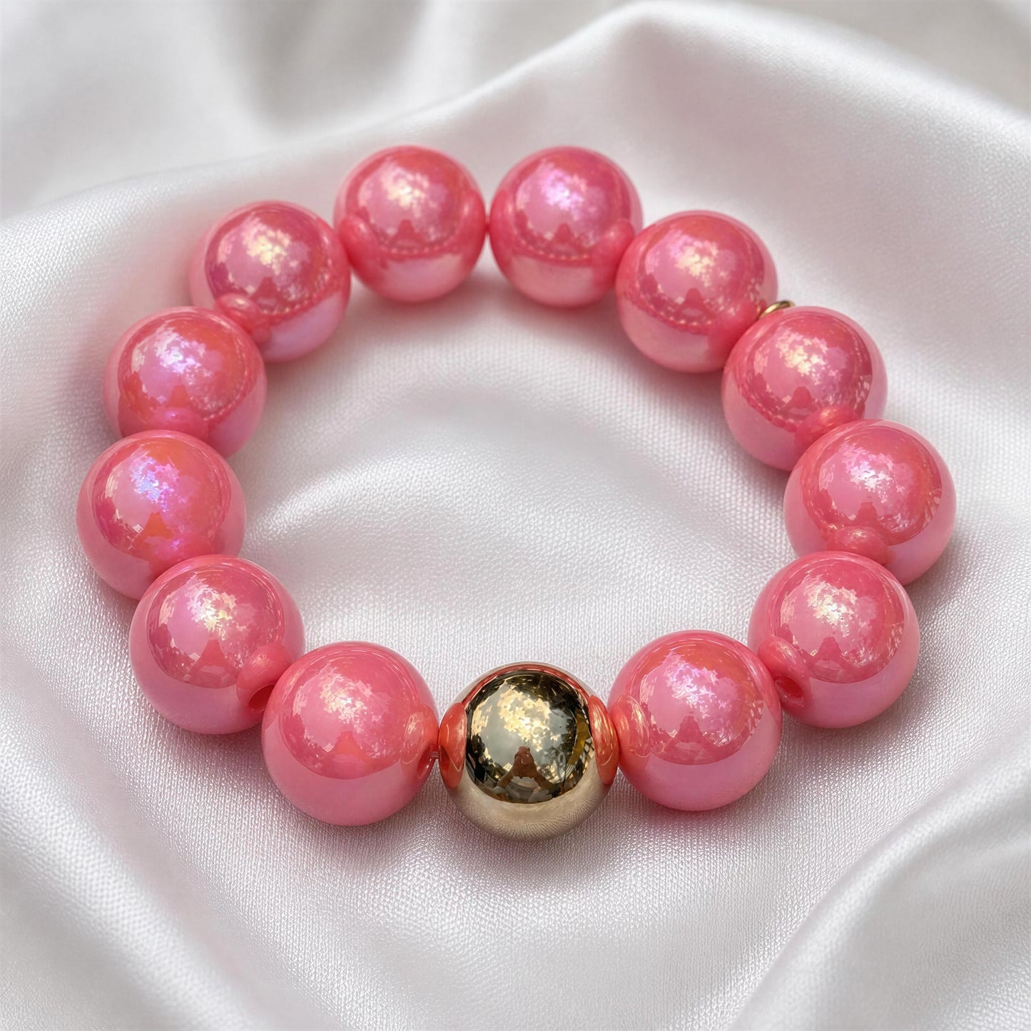 Pink beaded bracelet with a gold accent on a white fabric background
