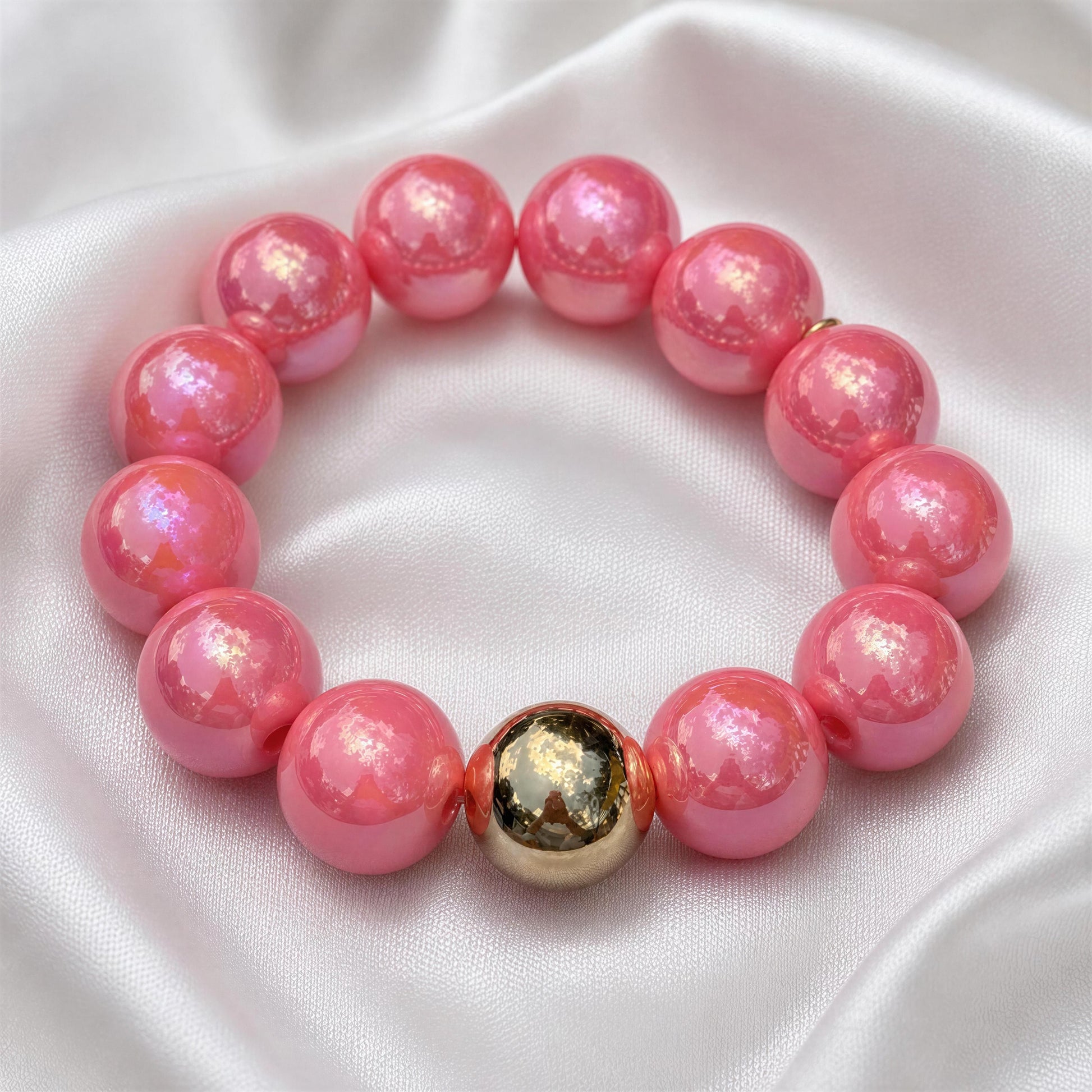 Pink beaded bracelet with a gold accent on a white fabric background