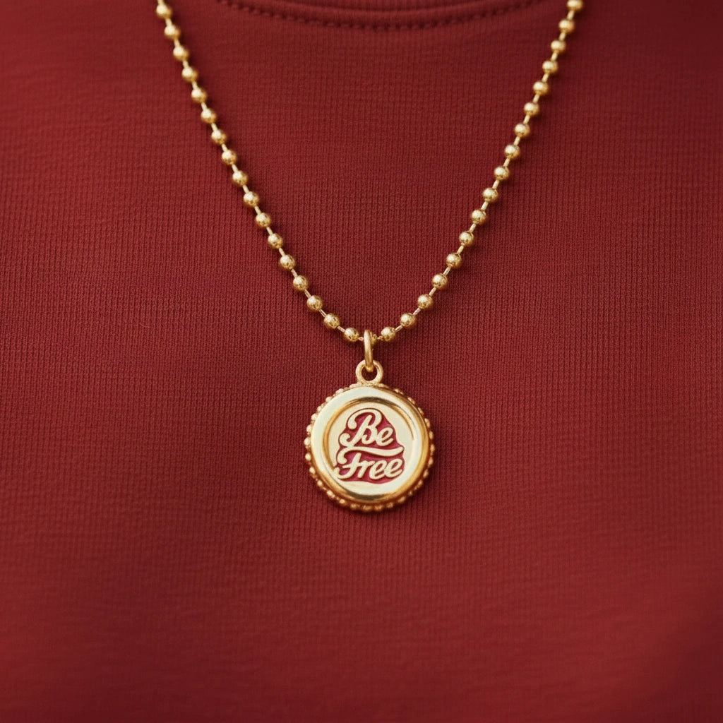 Gold necklace with 'Be Free' Chica Chica Jewelry pendant on a red background