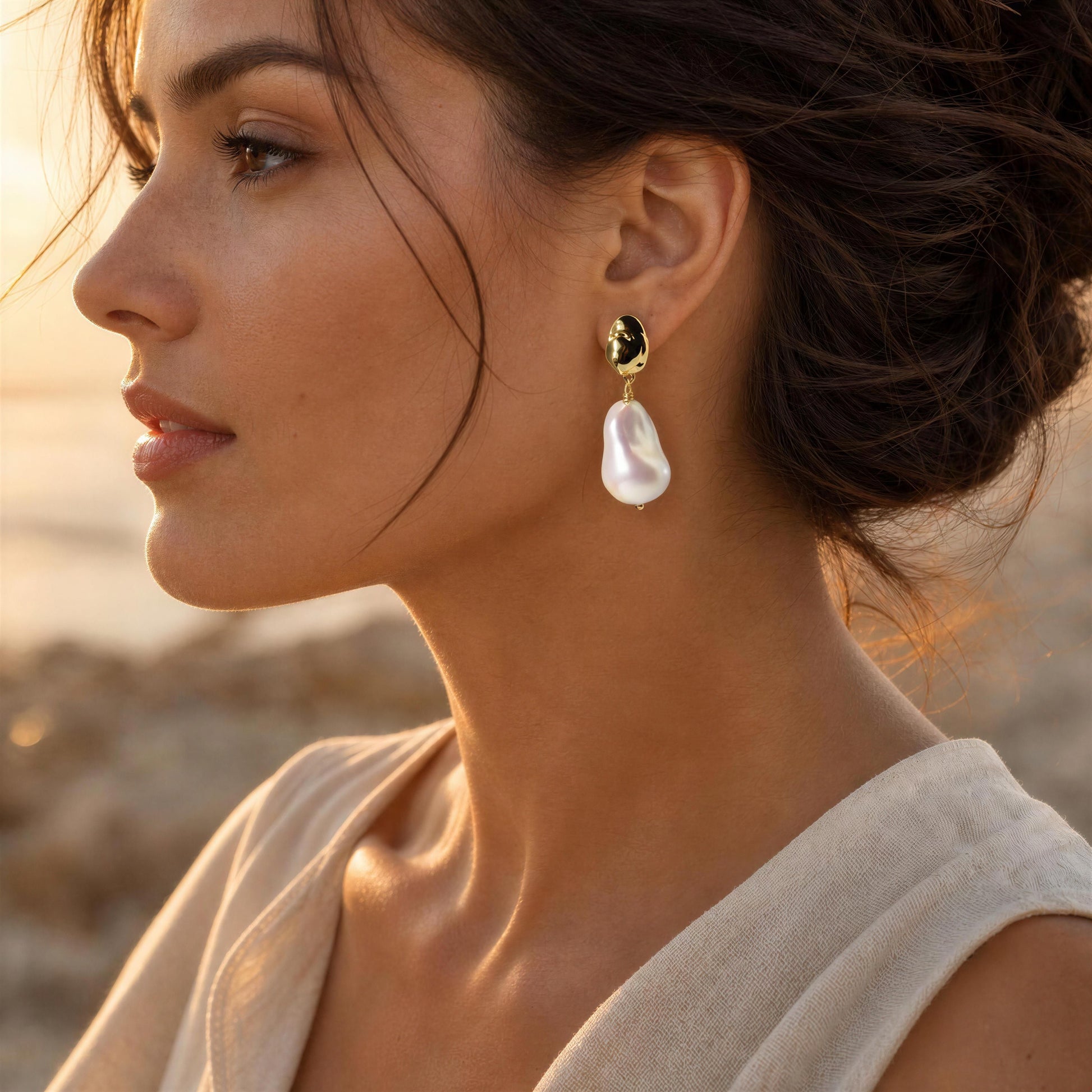 A woman in profile wearing the Bellina Pearl crop earrings from Chica Chica Jewelry, a gold drop earring with a white baroque pearl, photographed in warm golden hour light.