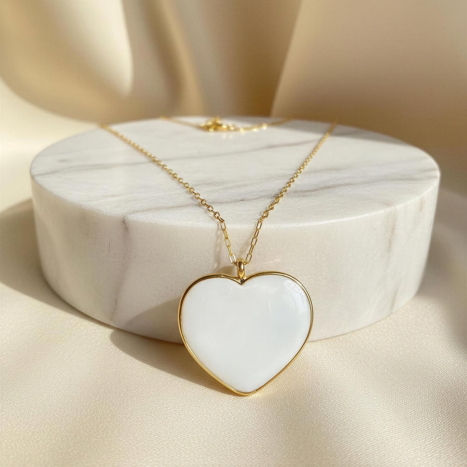 Heart-shaped necklace with white center and gold frame on a marble stand.
