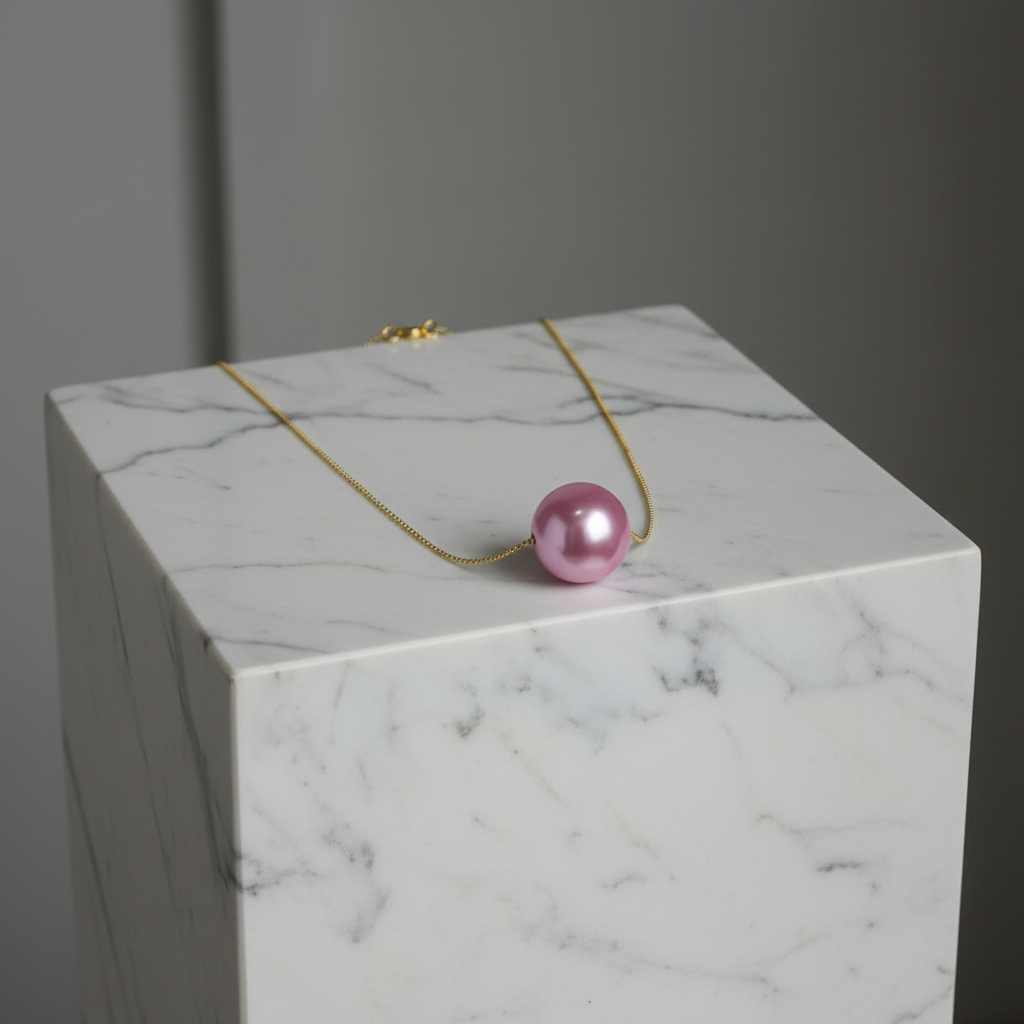 The Blush Petite Sphere Necklace on a marble surface with a gray background