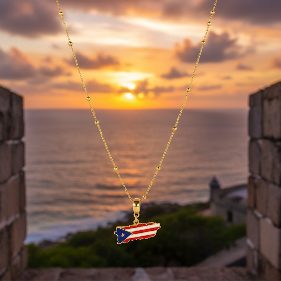 Borinquen Flag Necklace a Puerto Rican flag pendant against a sunset ocean backdrop by El Morro fortress.