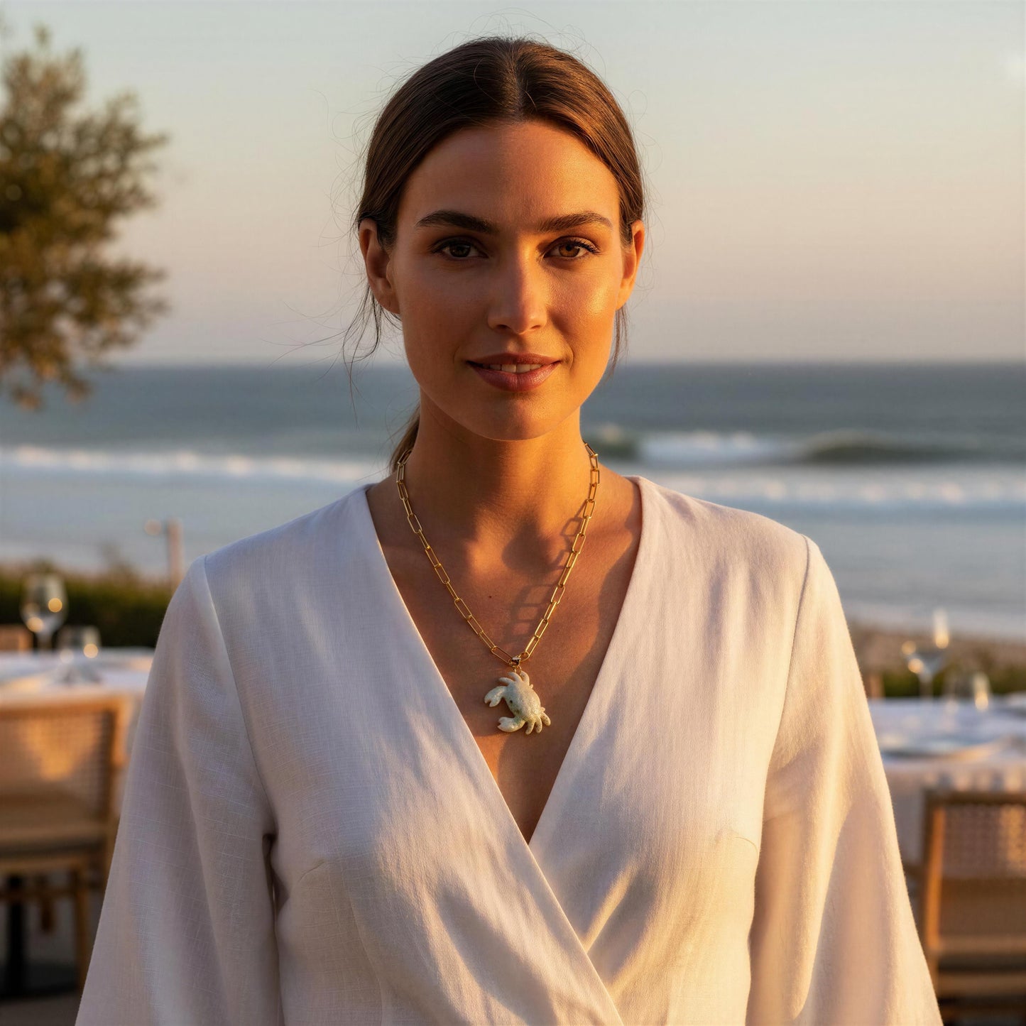 Woman in a white outfit with a scenic ocean view in the background wearing the Brisa Crab Necklace.