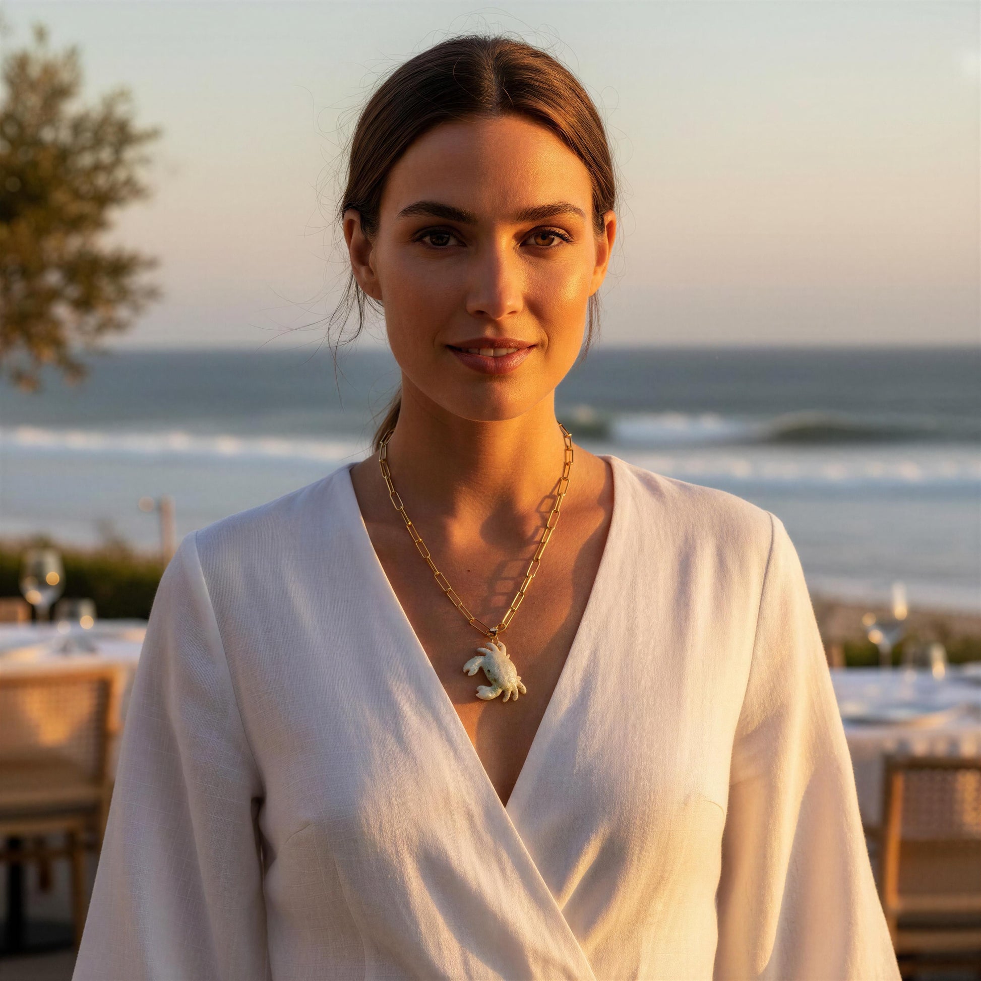 Woman in a white outfit with a scenic ocean view in the background wearing the Brisa Crab Necklace.