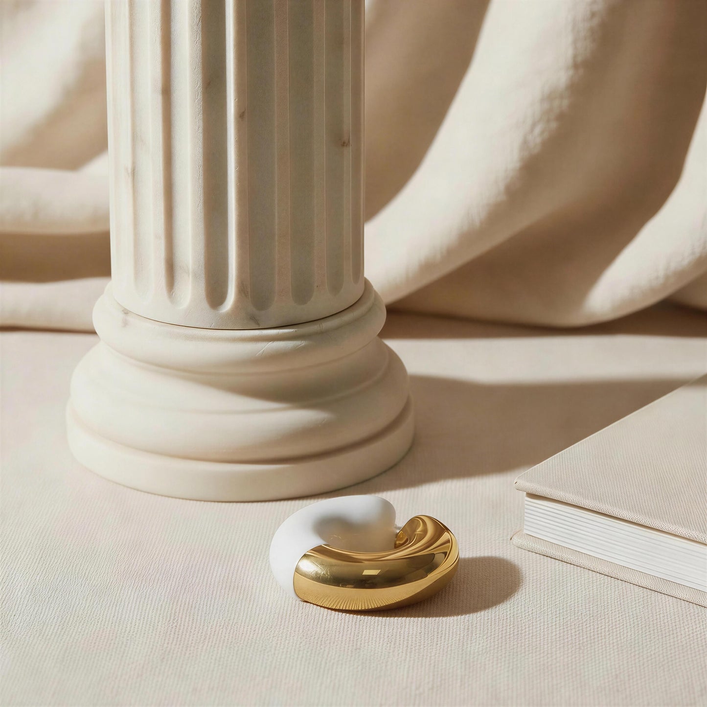 Decorative object with the Gatsby Arc Ear Cuff in Milky White on a beige surface with a column in the background