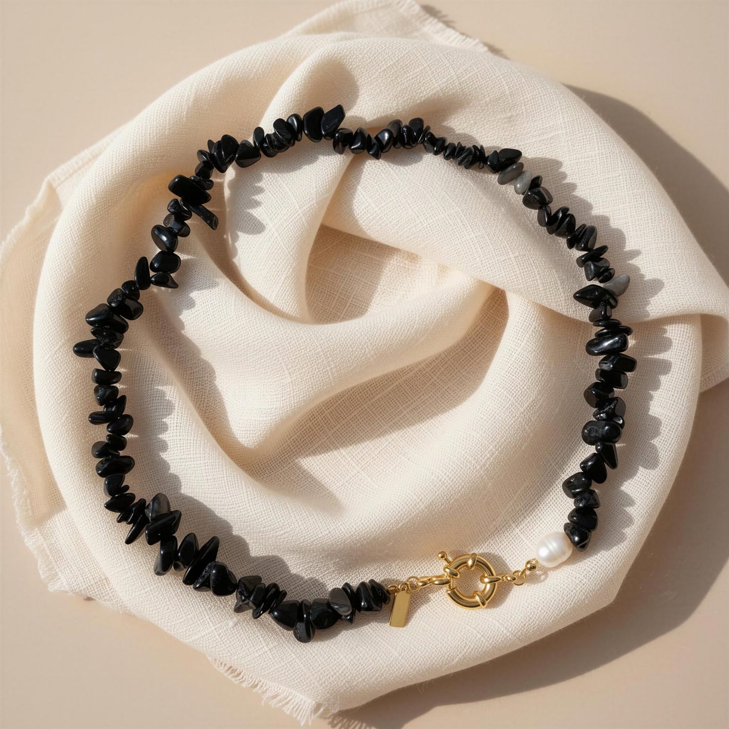 Black beaded bracelet with a gold clasp on a beige fabric background