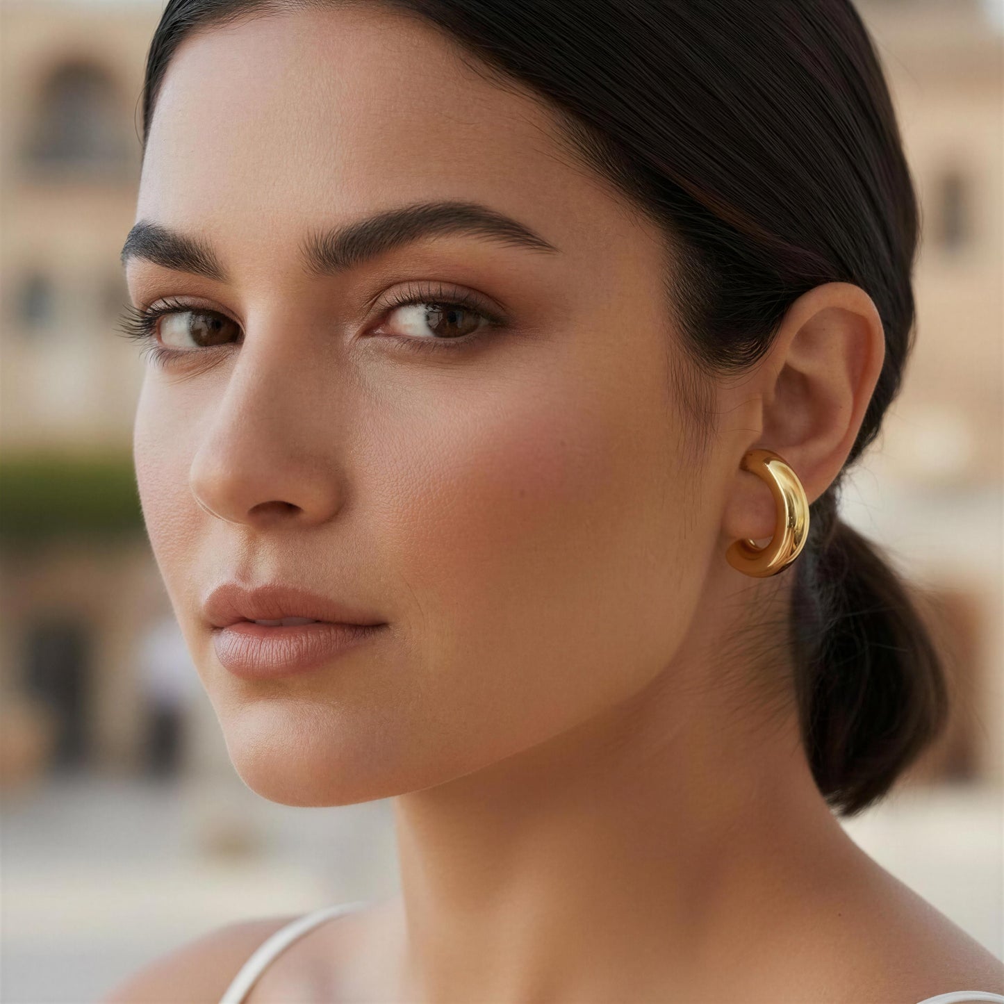 Close-up of a woman wearing gold hoop earrings with a blurred background