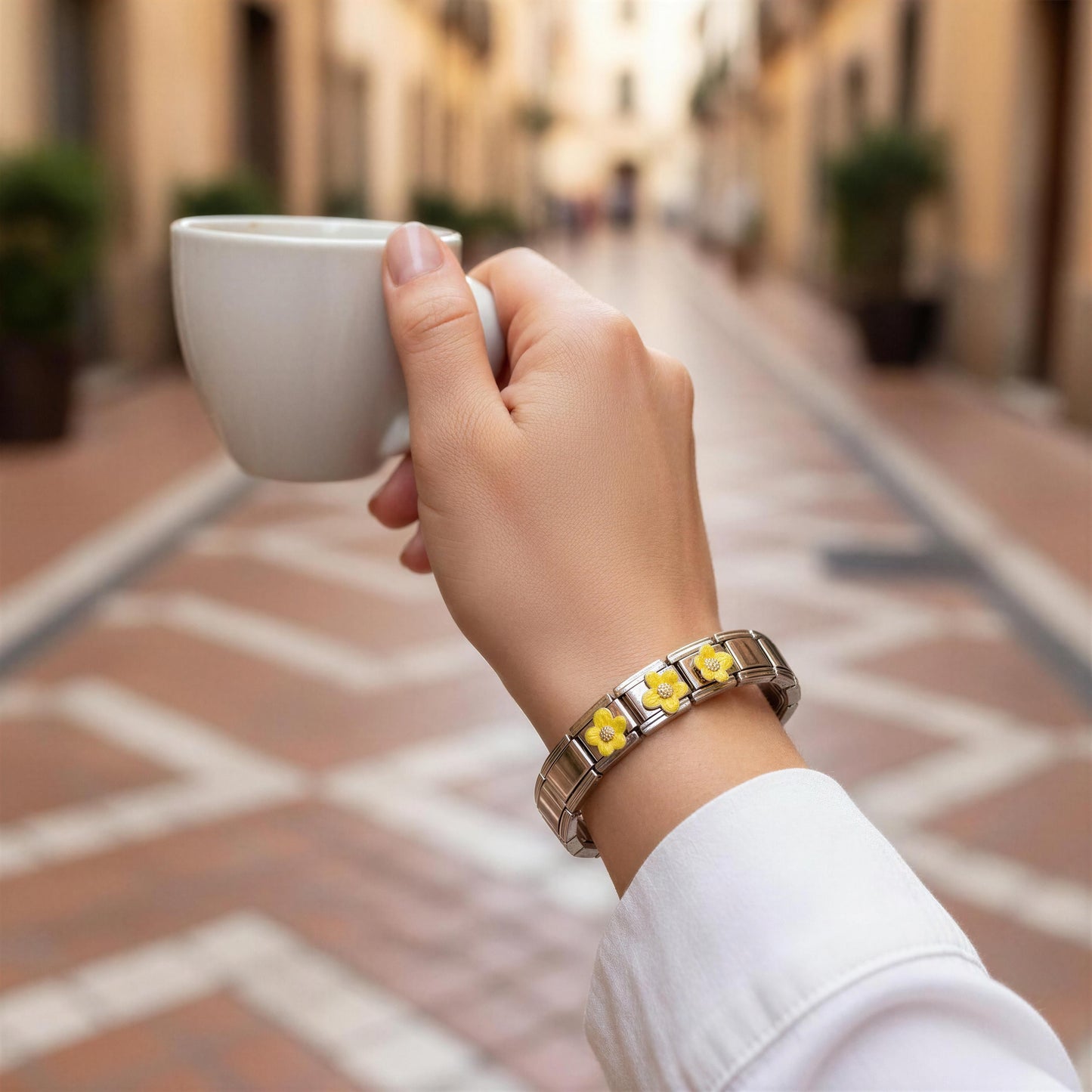 Hand holding a white cup with a blurred street scene in the background wearing the Sunlit Blossom Bracelet 