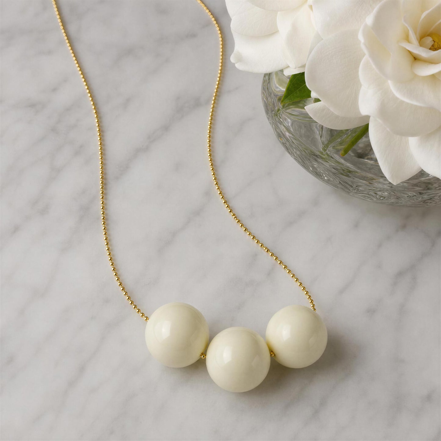 The Calla necklace with gold chain on a marble surface with white flowers.