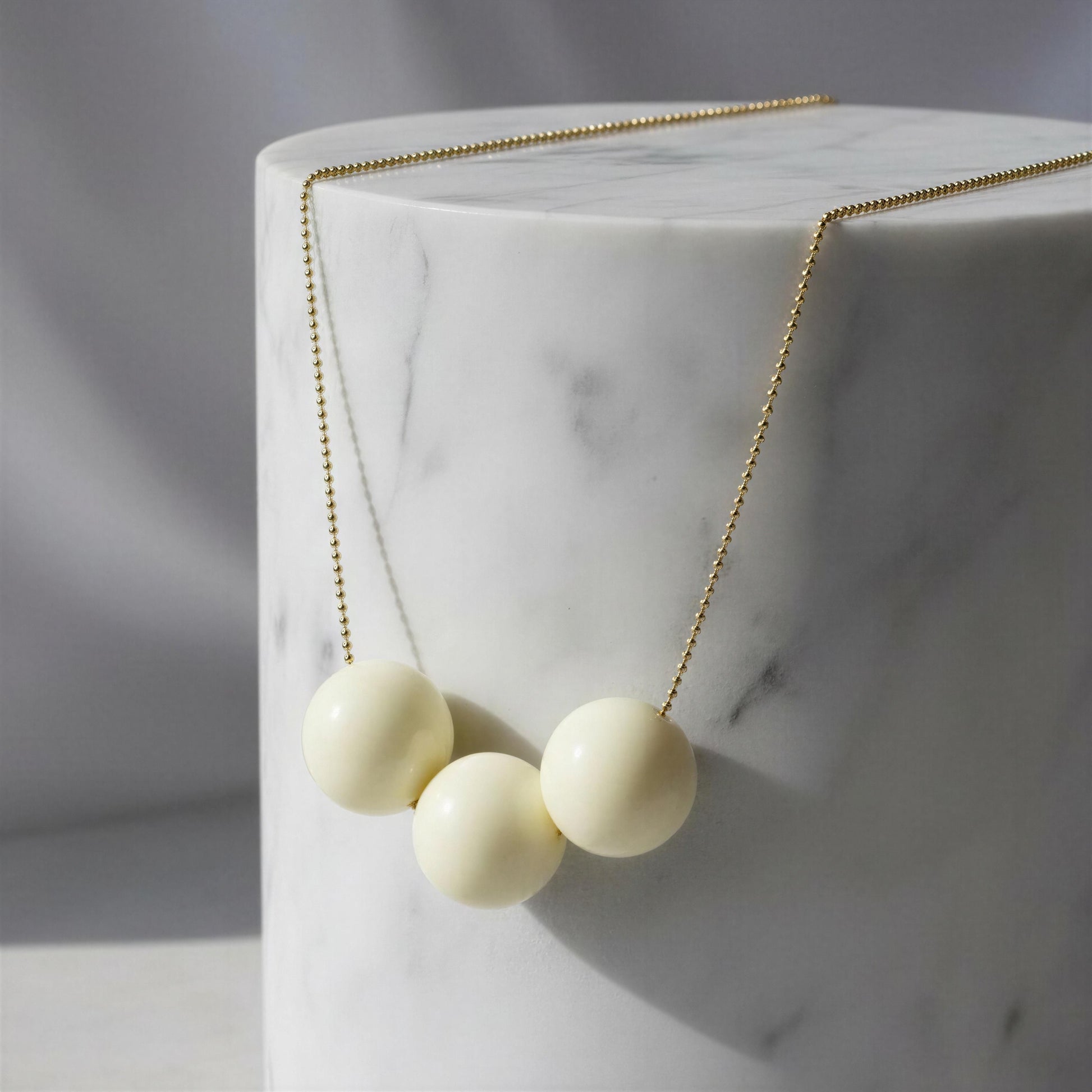Necklace with three cream-colored beads on a marble surface