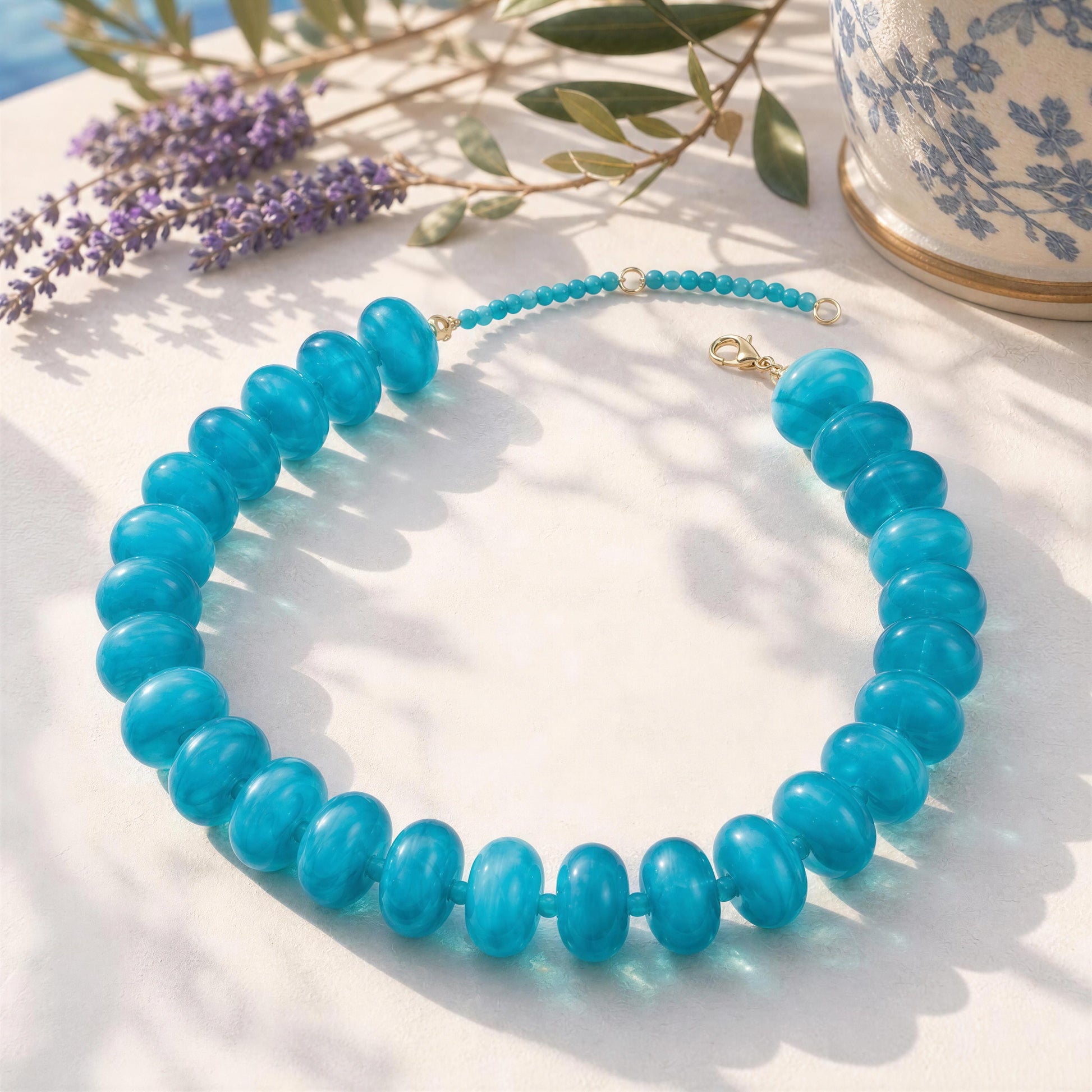 Turquoise resin beaded necklace from Chica Chica Jewelry on a light surface with lavender and a teacup in the background