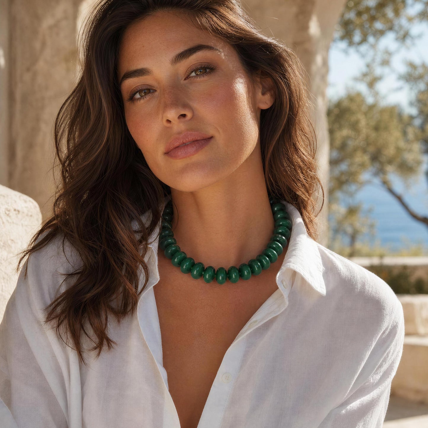 Woman wearing a green necklace outdoors with trees and clear sky in the background