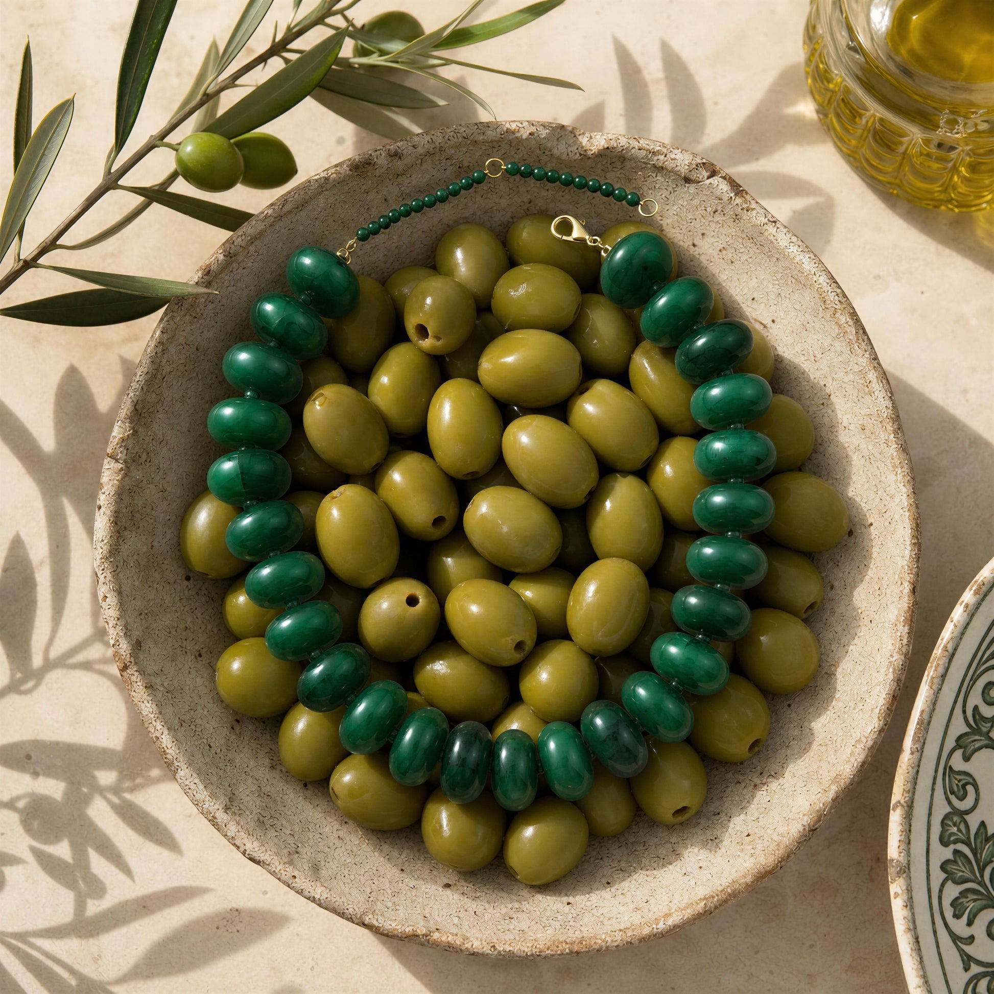 The Capri Verde Statement Choker in a bowl with olive branches and oil in the background