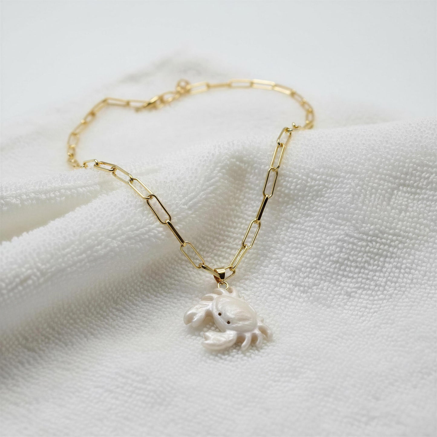 The Brisa Crab Necklace from Chica Chica Jewelry on a white towel background.