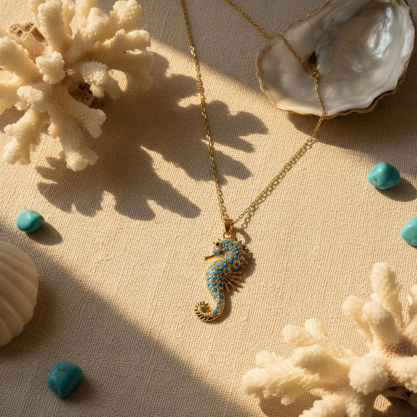 The Denizati Necklace from Chica Chica Jewelry, displayed on a textured beige fabric with seashell and coral props.