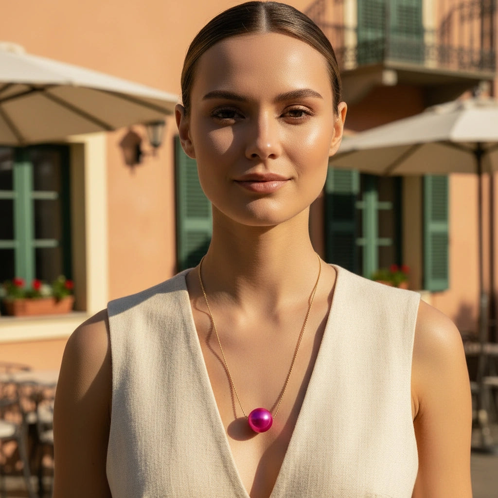 Woman wearing the Carmin Petite Sphere Necklace with a pink pendant outdoors