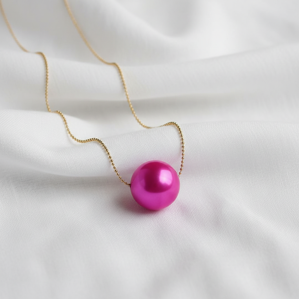 The pink Carmín Petite Sphere Necklace on a white fabric background