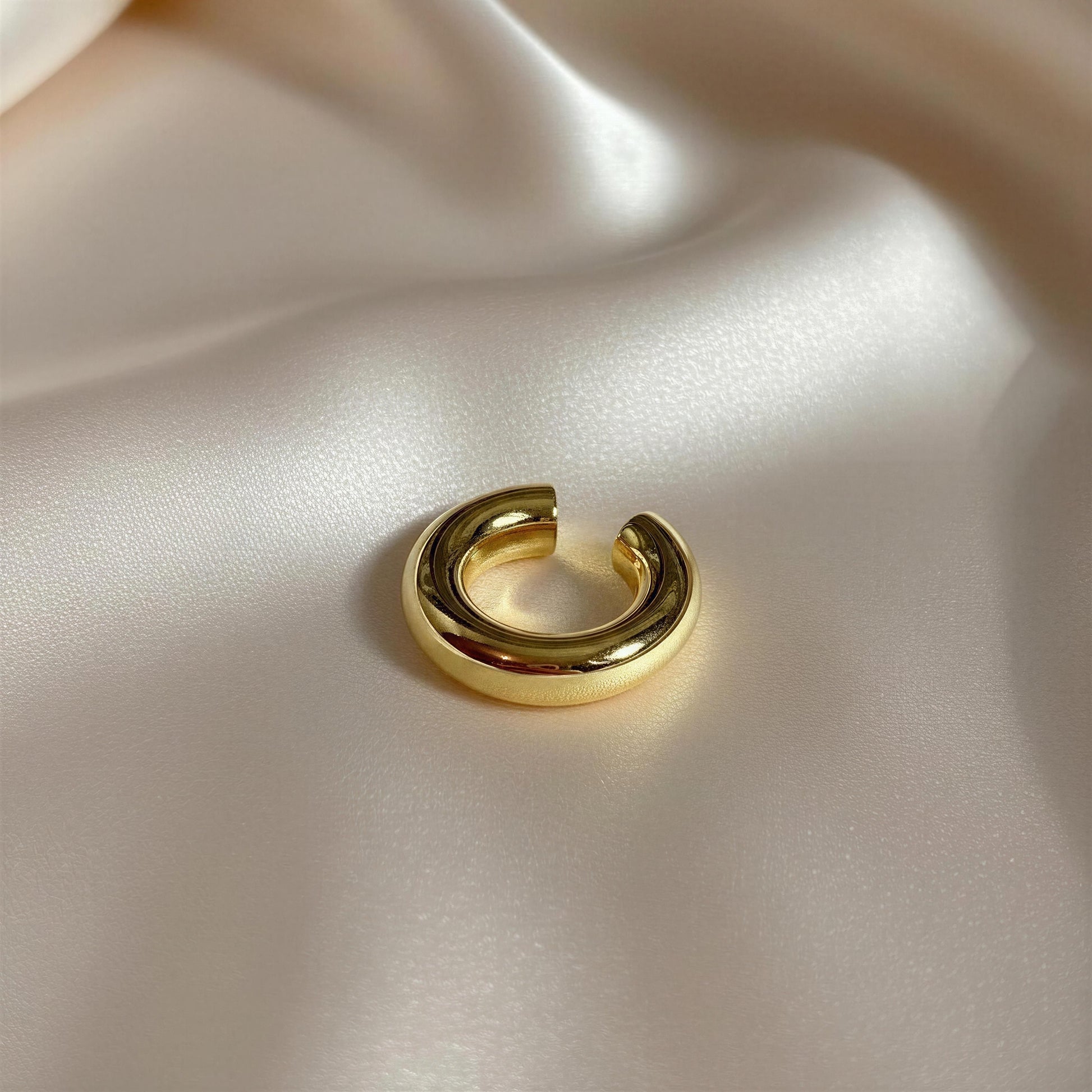 Gold hoop earring on a soft beige fabric background