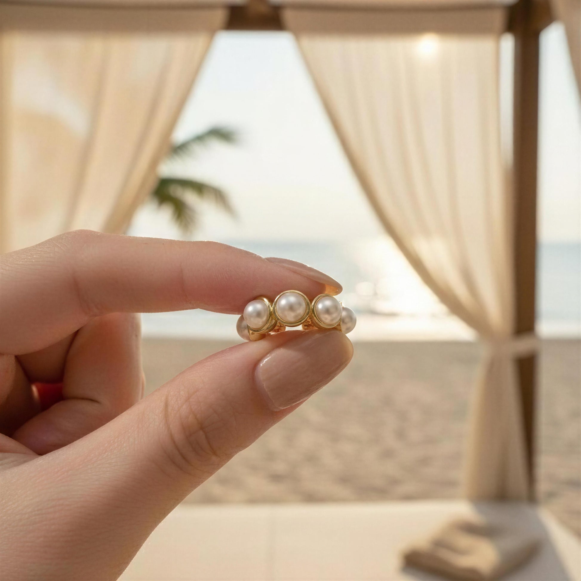 Hand holding the Celestial Pearl Cuff against a beach backdrop